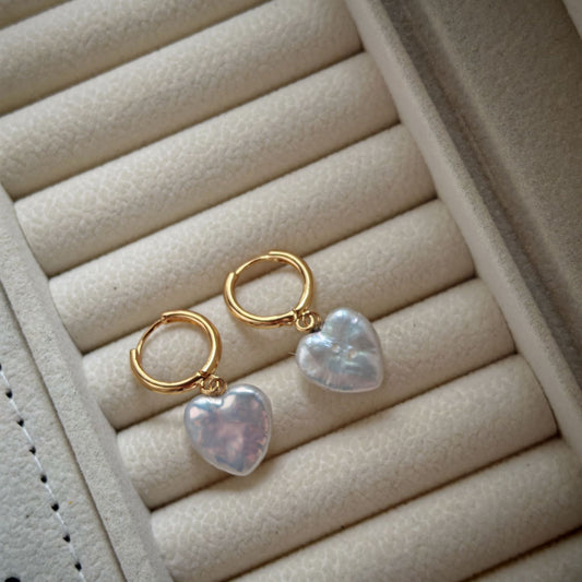Heart-shaped earrings with gold hoops on a beige jewelry display.