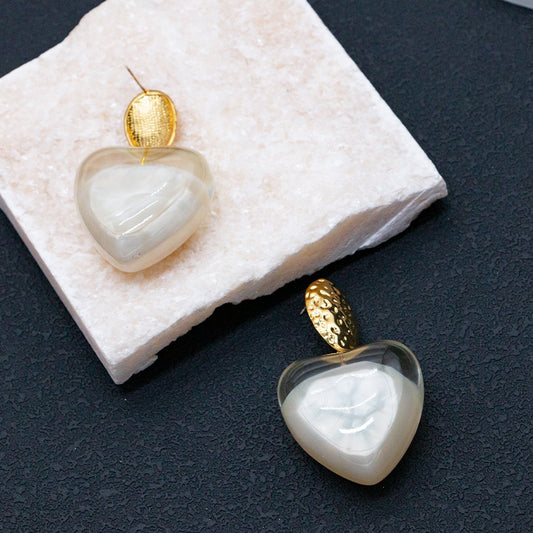 Heart-shaped earrings with gold tops on a textured white surface.